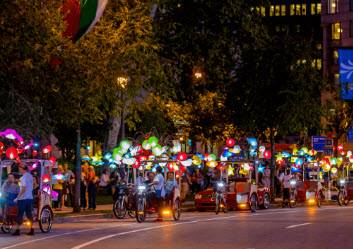 A street full of people riding rickshaws at night.