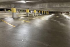 Empty, wet parking garage with yellow-striped spaces and concrete columns under artificial lighting.
