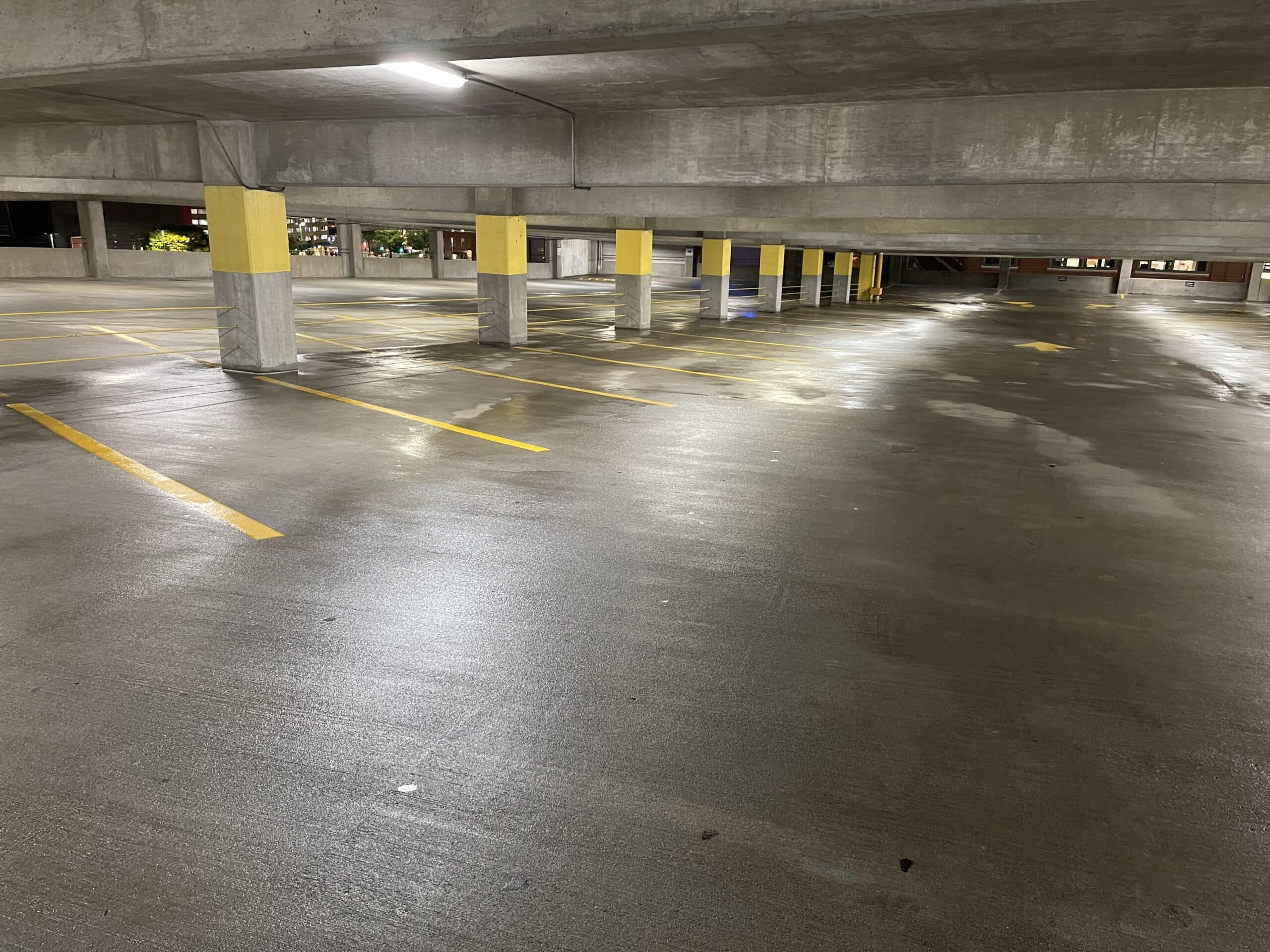 Empty, wet parking garage with yellow-striped spaces and concrete columns under artificial lighting.