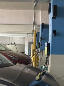 Electric vehicles parked in an indoor garage are connected to wall-mounted charging stations by black charging cables.