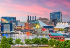 Baltimore Inner Harbor at sunset, featuring modern buildings, the National Aquarium, waterfront, boats, and colorful sky.