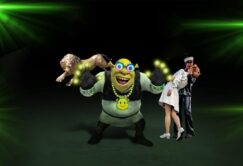 A cartoon ogre with glowing hands stands in the center, flanked by a bronze lion statue and two people posing, one in a white outfit and the other in dark attire, against a dark background.