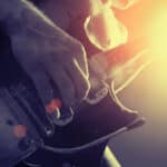 Close-up of a person playing an electric guitar, with sunlight and lens flare illuminating the scene from the right.