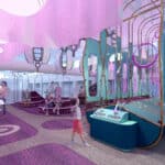Children and adults interact with various play structures and activity stations in a brightly lit, modern indoor play area with purple and blue decor.