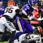 A Baltimore Ravens player attempts to catch a football while being defended by two Cincinnati Bengals players during a game.