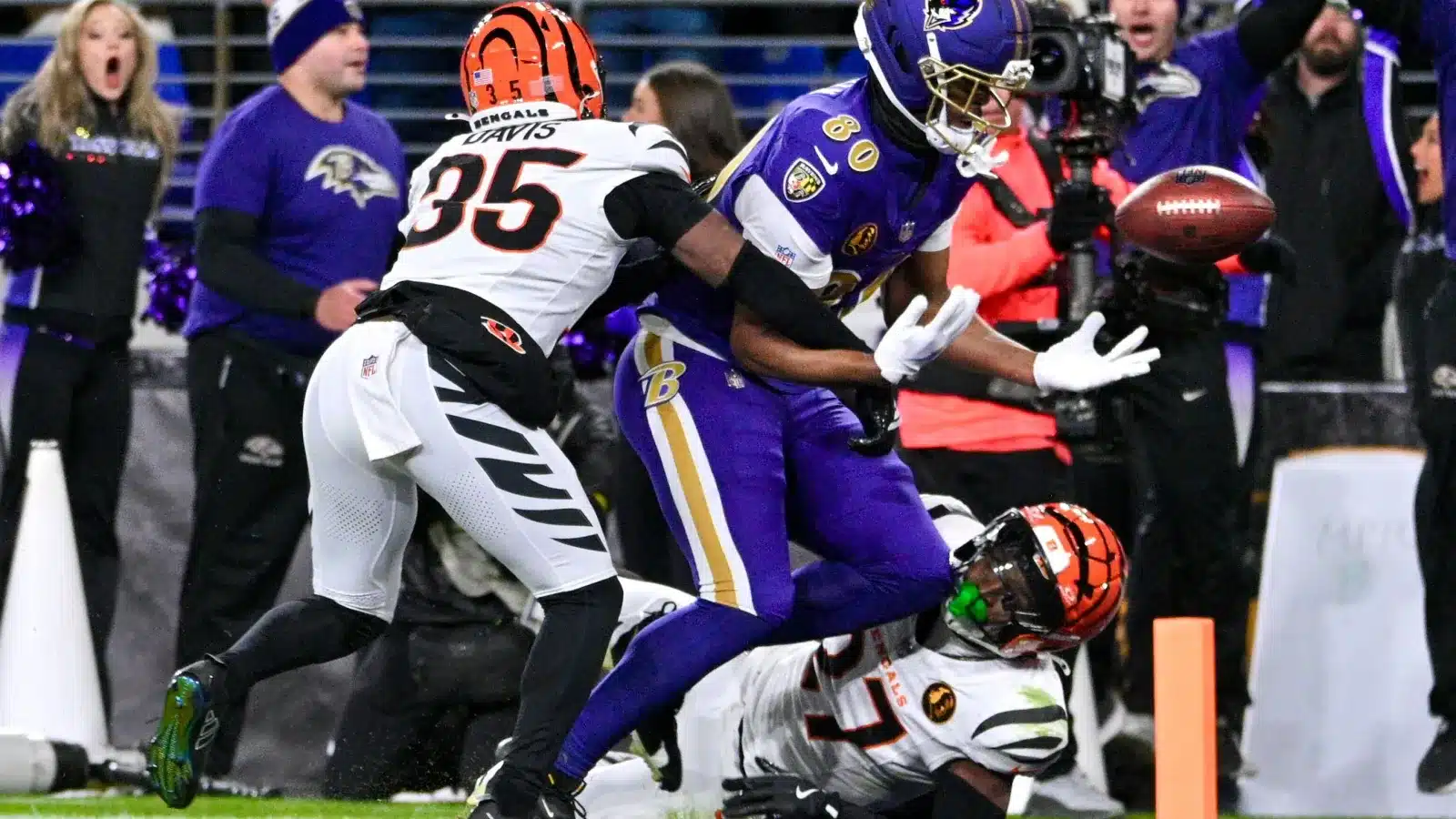 A Baltimore Ravens player attempts to catch a football while being defended by two Cincinnati Bengals players during a game.