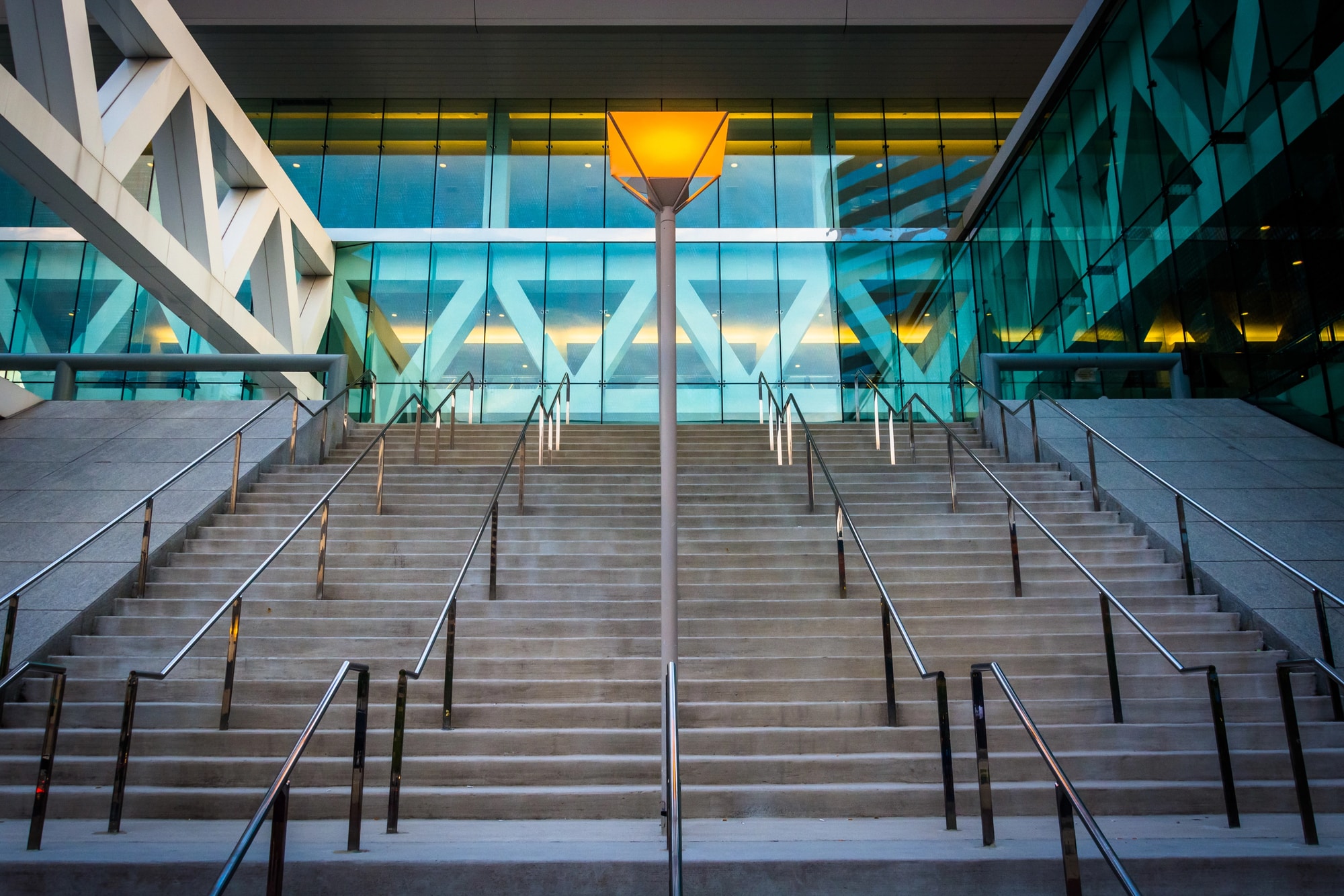 Wide concrete staircase with metal railings leads up to a modern glass Baltimore Convention Center; a single lit streetlamp stands at the center of the steps.