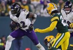 A Baltimore Ravens player runs with the football while being pursued by Green Bay Packers defenders during an NFL game.