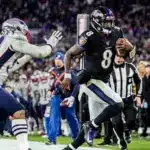 A Baltimore Ravens player runs with the football while being chased by a New England Patriots defender during an NFL game.